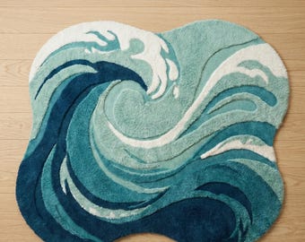 Puede incluir: Una alfombra de mechones con una forma orgánica irregular que presenta un diseño de olas oceánicas en capas. La alfombra muestra tonos de azul marino profundo, verde azulado y azul claro, acentuados con detalles blancos que representan la espuma.