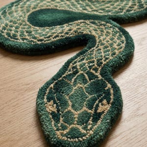 May include: A green and beige snake-shaped rug. The rug has a detailed design with varying shades of green and beige, creating a textured appearance. The snake's head is prominently displayed, with intricate patterns.