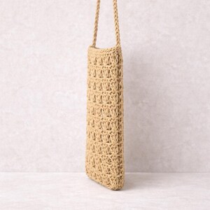 Pu&ograve; includere: Una borsa rettangolare beige all'uncinetto con una lunga tracolla intrecciata. La borsa presenta un motivo a trama aperta e strutturata. La tracolla &egrave; attaccata in alto, permettendo di indossarla a spalla o a tracolla. La borsa &egrave; vuota.