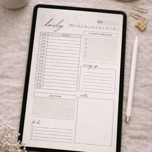 May include: A digital daily planner on a black tablet, featuring sections for time, activity, and notes. The planner includes the text "daily" and "date", with checkboxes and space for "good things" and "to do". A white stylus rests beside the tablet.