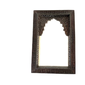 May include: A rectangular wall mirror featuring a dark brown wooden frame with intricate hand-carved floral patterns and a scalloped arch design at the top. The outer border of the frame displays a repeating textured pattern of small horizontal lines.