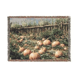 May include: A rectangular woven throw blanket featuring a detailed scene of a pumpkin patch. The design displays numerous orange pumpkins resting on the ground in front of a rustic wooden fence, with green foliage and corn stalks in the background.