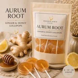 May include: A beige stand-up pouch labelled Aurum Root Ginger & Honey Lollipops containing individually wrapped amber-coloured round lollipops. Beside the pouch are a fresh ginger root, a wooden honey dipper in a bowl, and lemon slices.