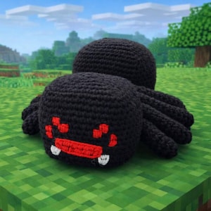 May include: A black crochet spider with red facial details and white fangs, resting on a green pixelated surface. The spider has eight legs and is set against a backdrop of a pixelated landscape, resembling a video game scene.