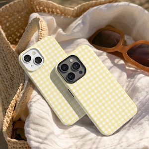 Peut inclure: Deux coques de téléphone portable arborant un motif à carreaux vichy jaune clair et blanc. Les coques présentent des découpes pour les objectifs de l'appareil photo arrière et sont placées ensemble, révélant le motif à carreaux uniforme.