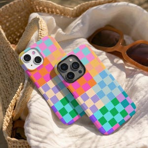 Könnte beinhalten: Zwei Smartphone-Hüllen mit einem lebendigen, mehrfarbigen Schachbrettmuster. Das Rasterdesign besteht aus Quadraten in den Farben leuchtendes Pink, Orange, Hellblau, Grün, Lila und Creme. Jede Hülle hat eine Aussparung für die Kamera.