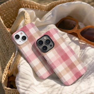 Puede incluir: Dos fundas para smartphone con un suave estampado de cuadros estilo acuarela en tonos rosa claro, rosa empolvado y crema. Cada funda tiene un recorte preciso para las lentes de la cámara trasera y un acabado mate suave en la superficie.