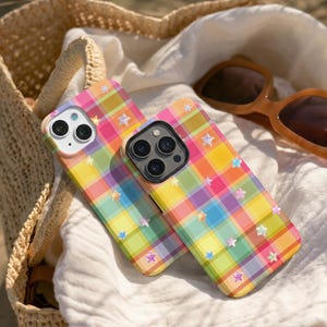May include: Two smartphone cases featuring a vibrant plaid pattern in shades of yellow, pink, green, and purple. The cases are decorated with small, scattered, iridescent star-shaped accents across the surface, each with a camera cutout.