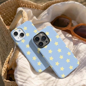 May include: Two light blue smartphone cases featuring a repeating pattern of small, pale yellow five-pointed stars. Each case has a cutout for a multi-lens camera system on the back, with one case showing two lenses and the other showing three lenses.