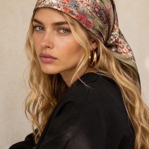 May include: A square headscarf featuring a multi-colored patchwork pattern with floral and geometric motifs in shades of green, red, blue, and cream. The scarf is tied over the head, displaying a smooth, satin-like texture and a solid olive green border.