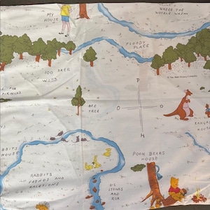 May include: A white fabric map featuring illustrations of Winnie the Pooh characters and locations. The map includes text such as "100 Aker Wood", "Pooh Bears House", and "Rabbit's House". The map has a blue river and green trees.