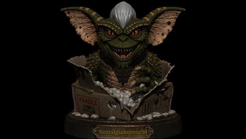 Puede incluir: Una criatura verde y escamosa con orejas grandes, ojos naranjas y un mech&oacute;n de pelo blanco que emerge de una caja de cart&oacute;n. La caja presenta el texto FRAGILE y HANDLE WITH CARE. Una placa en la base muestra el texto Nostalgiahorror3d en oro.