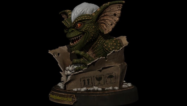 Puede incluir: Una criatura verde y escamosa con orejas grandes, dientes afilados y pelo blanco que emerge de una caja de cart&oacute;n rota. La caja tiene tres iconos de env&iacute;o negros y se asienta sobre una base circular con una placa dorada NightHorror3d.