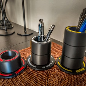 Könnte beinhalten: Ein Set aus drei Keramikbechern mit gesprenkelter, matter Oberfläche. Die Becher sind in den Farbtönen Creme, Hellgrau und Dunkelgrau gehalten. Jeder Becher hat ein schlichtes, minimalistisches Design und einen abgerundeten Henkel.