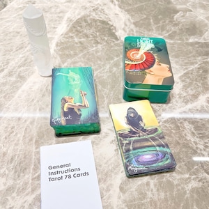 May include: A tarot card deck with a green and white box, a clear crystal, and a booklet. The tarot cards feature colorful illustrations of figures and scenes. The box is labeled "The Light Seer's Tarot". The booklet reads "General Instructions Tarot 78 Cards".