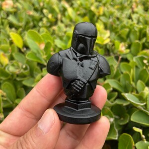 Op de afbeelding: Een zwarte buste van een personage uit een sciencefictionreeks. De figuur draagt een helm en harnas, met een gedetailleerd borststuk en een riem over de torso. De buste is gemonteerd op een cirkelvormige basis.
