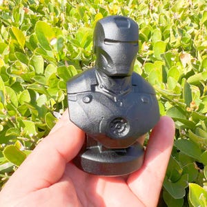 Puede incluir: Busto negro de un superh&eacute;roe con casco y armadura pectoral. El busto est&aacute; hecho de un material s&oacute;lido y tiene un acabado mate. Es un art&iacute;culo de colecci&oacute;n.