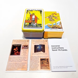 Puede incluir: Un juego de cartas del tarot con una caja amarilla y negra con la ilustración de la carta "El Mago", una baraja de cartas con la ilustración de la carta "El Loco" y tarjetas de instrucciones. También se incluyen dos tarjetas con detalles del libro y un folleto.