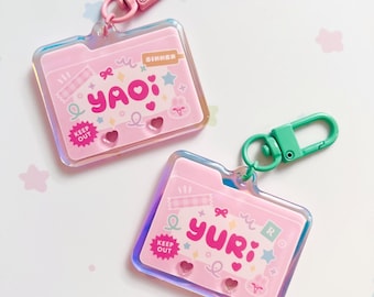 Può includere: Due portachiavi rosa in acrilico a forma di cartella, con bordi iridescenti e chiusure abbinate. Un portachiavi ha il nome "Yao" e l'altro "Yuri" in lettere rosa. Ogni portachiavi ha elementi decorativi e la scritta "Keep Out".