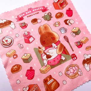 May include: Pink fabric featuring a repeating pattern of baked goods, bunnies, and kitchen tools. A brown bunny bakes in a pink bowl. The words "Bun Bun Bakery" are on a banner. Other items include bread, a teapot, and a scale.