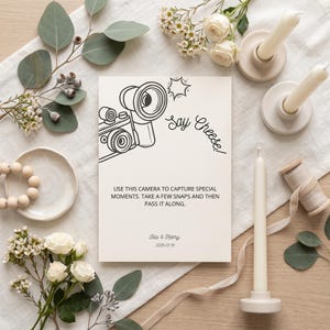 May include: A rectangular white card featuring a black line drawing of a camera, the text "Say Cheese!", and the printed instruction "USE THIS CAMERA TO CAPTURE SPECIAL MOMENTS. TAKE A FEW SNAPS AND THEN PASS IT ALONG." with "Isla & Harry" and "2026.05.15".