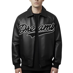 Peut inclure: Veste en cuir noire avec le mot "Dreams" en écriture blanche sur la poitrine. La veste a un col, une fermeture éclair et des poignets et un ourlet côtelés. Un vêtement d'extérieur élégant.