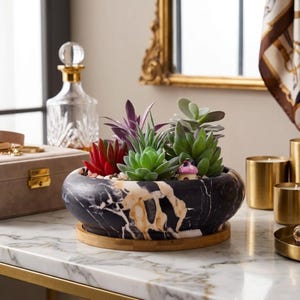 May include: A round, black and white marble-patterned planter bowl resting on a circular bamboo base. The planter contains a variety of artificial succulents in shades of green, red, and purple, along with a small decorative pink mushroom figurine.