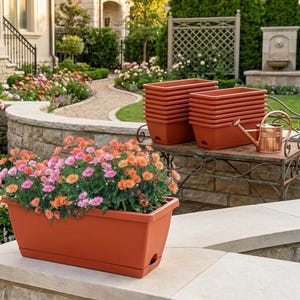 Może przedstawiać: Kilka prostokątnych donic w kolorze terakoty jest ułożonych w stos i wystawionych na zewnątrz. Jedna donica jest wypełniona różowymi i pomarańczowymi kwiatami. Widać również miedzianą konewkę. Scena rozgrywa się w ogrodzie.