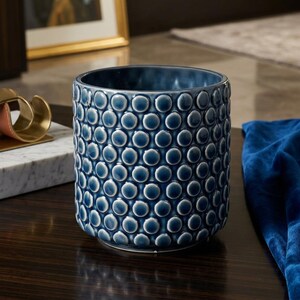 Peut inclure: Un vase cylindrique en céramique bleu foncé avec un motif de points en relief texturés. Le vase est posé sur une surface en bois sombre. C'est un objet décoratif pour la maison.