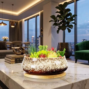 May include: A low, round ceramic planter with a speckled brown and white glaze, filled with a variety of green and reddish succulents. The planter sits on a circular light-coloured wooden base, showcasing a textured finish and a wide, open top.
