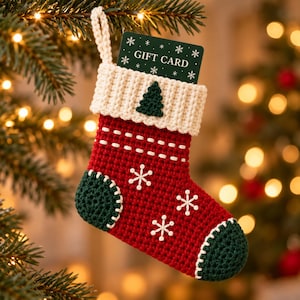 May include: A red and green crocheted Christmas stocking with a white cuff featuring a small green tree. The stocking is decorated with white stitched snowflakes and contains a dark green gift card with white snowflake patterns and text.