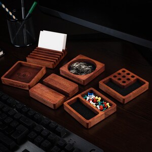 Op de afbeelding: Een verzameling houten bureau-organizers in verschillende vormen en maten. Inclusief een visitekaarthouder, vierkante trays, een tray met punaises en een tray met paperclips. Het hout heeft een warme, roodbruine tint.