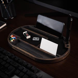 May include: A dark wood desk organizer with multiple compartments. It holds a smartphone, pen, business cards, push pins, and a pencil eraser. The organizer has the engraved text: "What is meant for you will always find you."