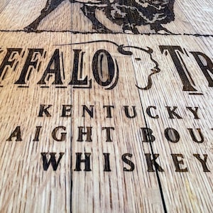 May include: Close-up of a wooden surface with the words "BUFFALO TRACE KENTUCKY STRAIGHT BOURBON WHISKEY" etched into the wood. A detailed image of a bison is above the text. The wood has a natural grain.