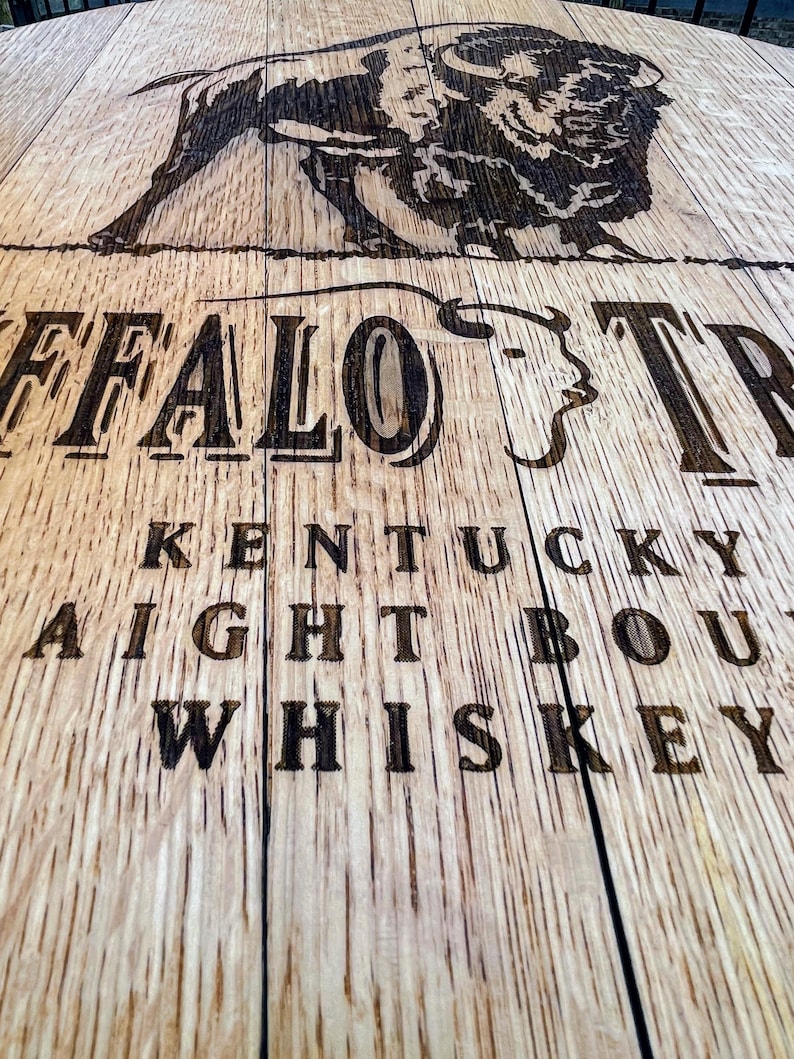 May include: Close-up of a wooden surface with the words "BUFFALO TRACE KENTUCKY STRAIGHT BOURBON WHISKEY" etched into the wood. A detailed image of a bison is above the text. The wood has a natural grain.