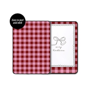 Może przedstawiać: Prostokątna naklejka na czytnik e-booków w czerwono-różową kratkę typu gingham. Jedna strona zawiera napis "in my Kindle era" oraz ręcznie rysowaną kokardkę w falistej ramce. Czarna okrągła etykieta zawiera tekst "Easy to peel and stick."