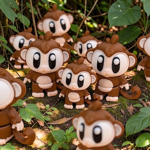 Pode incluir: Uma coleção de figuras de macacos em tons de castanho e creme com olhos grandes e expressivos e caudas enroladas. Cada figura apresenta uma cabeça lisa e arredondada, orelhas proeminentes e um corpo pequeno, dispostas em grupo.