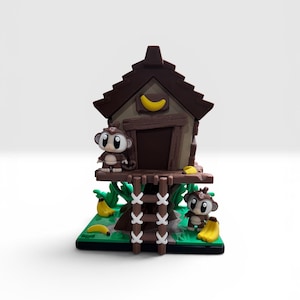 May include: A brown treehouse figurine featuring a dark brown roof with a yellow crescent moon accent. Two small monkey figures with large eyes are positioned on the structure, surrounded by green foliage and several yellow banana pieces.