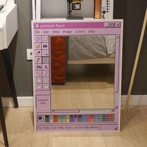 Può includere: Uno specchio rettangolare incorniciato per assomigliare a una finestra di un classico programma di pittura per computer, con un bordo rosa e una varietà di icone e testo. Il testo recita "untitled-Paint" e "Custom text".