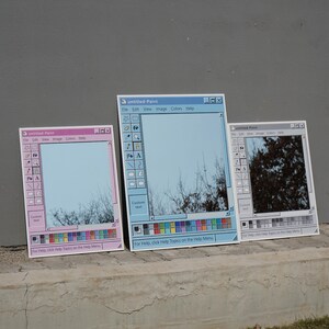 Puede incluir: Tres espejos dise&ntilde;ados para parecerse a la ventana de la aplicaci&oacute;n "untitled-Paint". Los espejos son de color rosa, azul y gris, con una barra de herramientas y una paleta de colores. El texto "untitled-Paint" y otras opciones de men&uacute; son visibles. Los espejos reflejan el cielo y los &aacute;rboles.