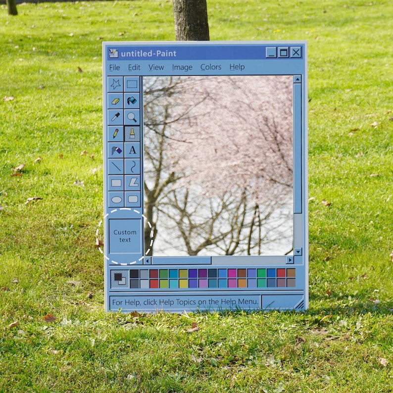 Op de afbeelding: Een lichtblauw, rechthoekig bord dat de klassieke Windows Paint-interface nabootst. Het toont een schilderachtig uitzicht op bomen met roze bloesems. De woorden "untitled-Paint" en "Custom text" zijn zichtbaar.
