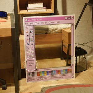 Puede incluir: Espejo rectangular enmarcado para parecerse a una interfaz de programa de pintura inform&aacute;tica. El marco rosa claro presenta una barra de men&uacute; y una paleta de colores. El texto "untitled-Paint" es visible.