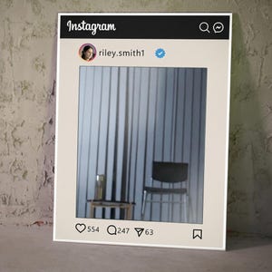 May include: A framed artwork designed to resemble an Instagram post. The top features the Instagram logo and a search icon. The post includes a profile picture, username, and a verified checkmark. The image within the frame shows a room with a chair and a table.