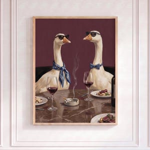 Può includere: Una stampa artistica incorniciata raffigura due oche a tavola, con occhiali da sole e cravatte, che si godono un pasto con vino. Una sigaretta è appoggiata in un posacenere. Lo sfondo è bordeaux scuro.