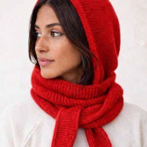 May include: A bright red knitted hooded scarf featuring a thick, textured ribbed stitch pattern. The accessory combines a deep hood with long, integrated scarf ends that wrap around the neck, providing full coverage with a consistent vibrant red yarn.