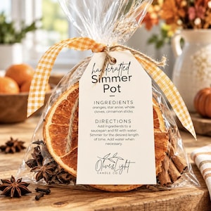 May include: A clear plastic bag containing dried orange slices, star anise, whole cloves, and cinnamon sticks. A white tag is tied with a yellow and white gingham ribbon, featuring the text Handcrafted Simmer Pot, ingredients, and directions.