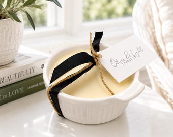 May include: A white ceramic ramekin filled with pale yellow candle wax. The container features a black ribbon and a jute twine string tied around it, holding a white rectangular tag printed with the text Olive & Light Candle Co.