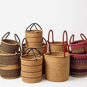 May include: A collection of woven baskets in various sizes and designs. The baskets are primarily tan with black or red accents on the handles and decorative stripes. Some baskets are striped, while others have solid colors.