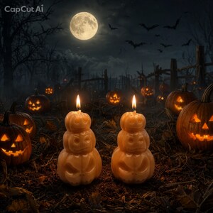 May include: Two stacked pumpkin-shaped candles with carved faces and lit wicks, positioned in a dark outdoor setting with a full moon, flying bats, and several other glowing jack-o'-lanterns scattered across the ground in the background.