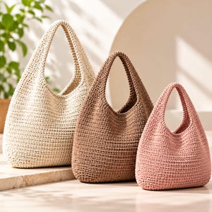 May include: Three hobo-style bags crafted from a textured, woven material. The bags are arranged in a row, featuring a large cream-colored bag, a medium-sized brown bag, and a smaller pink bag, each with a single integrated handle and open top.